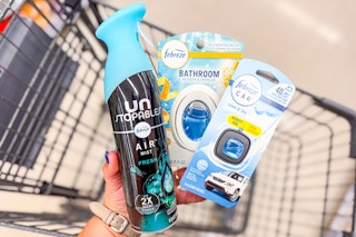 person holding febreze air freshener, small spaces, and car vent clip over a cart