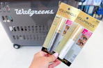 hand holding two loreal mascaras in front of a walgreens shopping basket