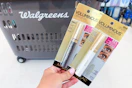hand holding two loreal mascaras in front of a walgreens shopping basket