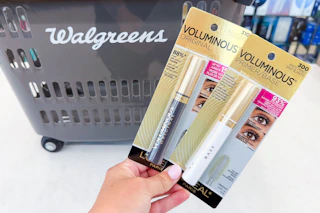 hand holding two loreal mascaras in front of a walgreens shopping basket