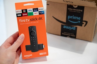 a hand holding an amazon fire stick box up next to an amazon prime package