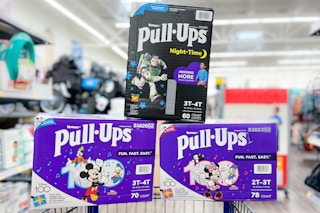 three boxes of Huggies Pull-Ups stacked on the rim of a Walmart cart in the baby aisle