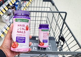 hand holding bottle of Nature's Bounty hair, skin, and nails advanced gummies in front of shopping cart