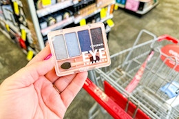 person holding a covergirl eyeshadow kit over a cvs cart