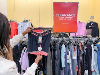 A woman holding a pair of Under Armour shorts next to a clearance sign