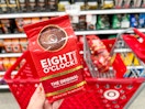 hand holding one bag of Eight O'Clock ground coffee in front of Target cart with more coffee bags inside