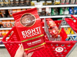 hand holding one bag of Eight O'Clock ground coffee in front of Target cart with more coffee bags inside