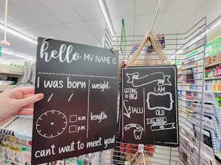 hand holding a chalkboard sign that you fill in birth information for a baby, by a first day of school chalkboard