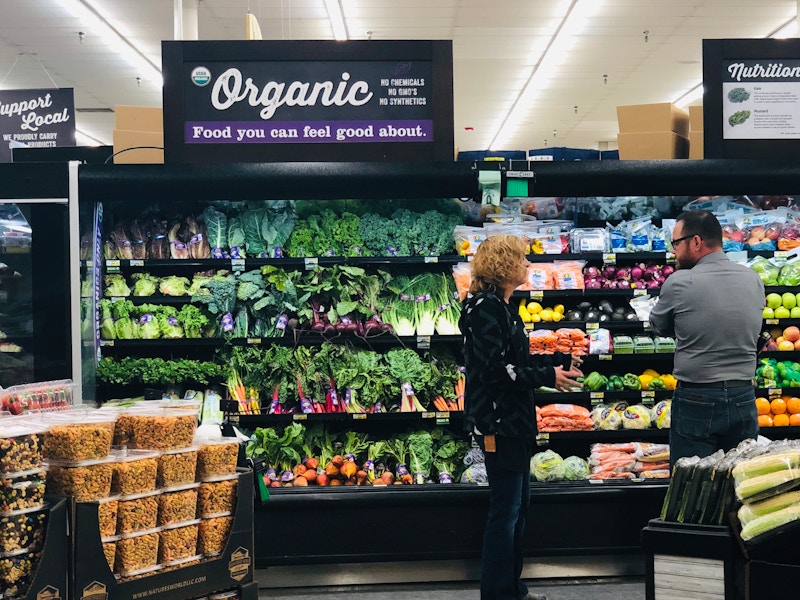 Two people talking in the produce section of a grocery store.