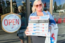A person holding a stack of dominos pizza boxes in front of a dominos store front