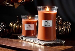 two pumpkin candles burning on a wooden surface