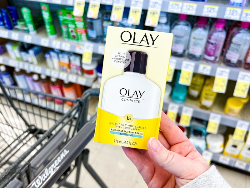 person holding an olay moisturizer over a walgreens cart