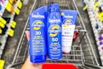 person holding 3 coppertone sunscreens over a cart