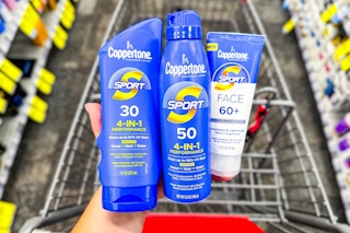person holding 3 coppertone sunscreens over a cart