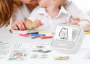 a sticker printer on a table with sticker sheets with a mom and little kid at a table