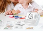 a sticker printer on a table with sticker sheets with a mom and little kid at a table