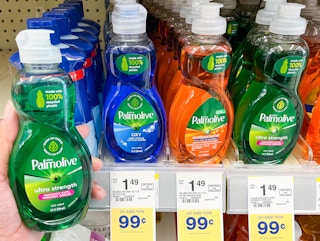 A person's hand holding a bottle of Palmolive Ultra Strength liquid dish soap next to a shelf of different variations of Palmolive liquid...