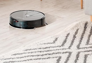 a robot vacuum on a floor next to a rug