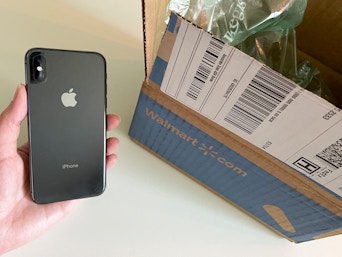An iPhone held next to an open walmart.com delivery box