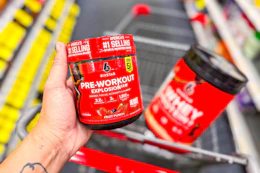 person holding six star pre workout over a cart with protein powder in it