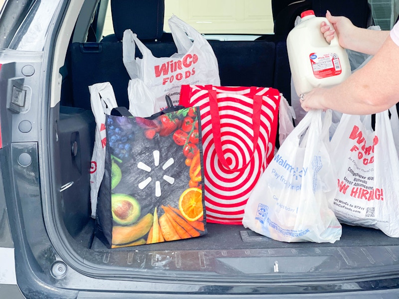 A person putting a gallon of milk into the trunk of a vehicle with reusable and plastic grocery bags from Walmart, Target, and WinCo Food...