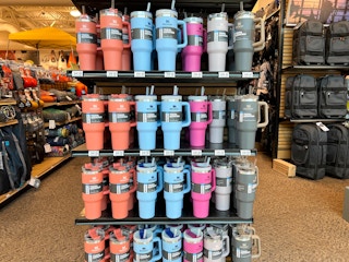 A shelf filled with Stanley big grip cups.