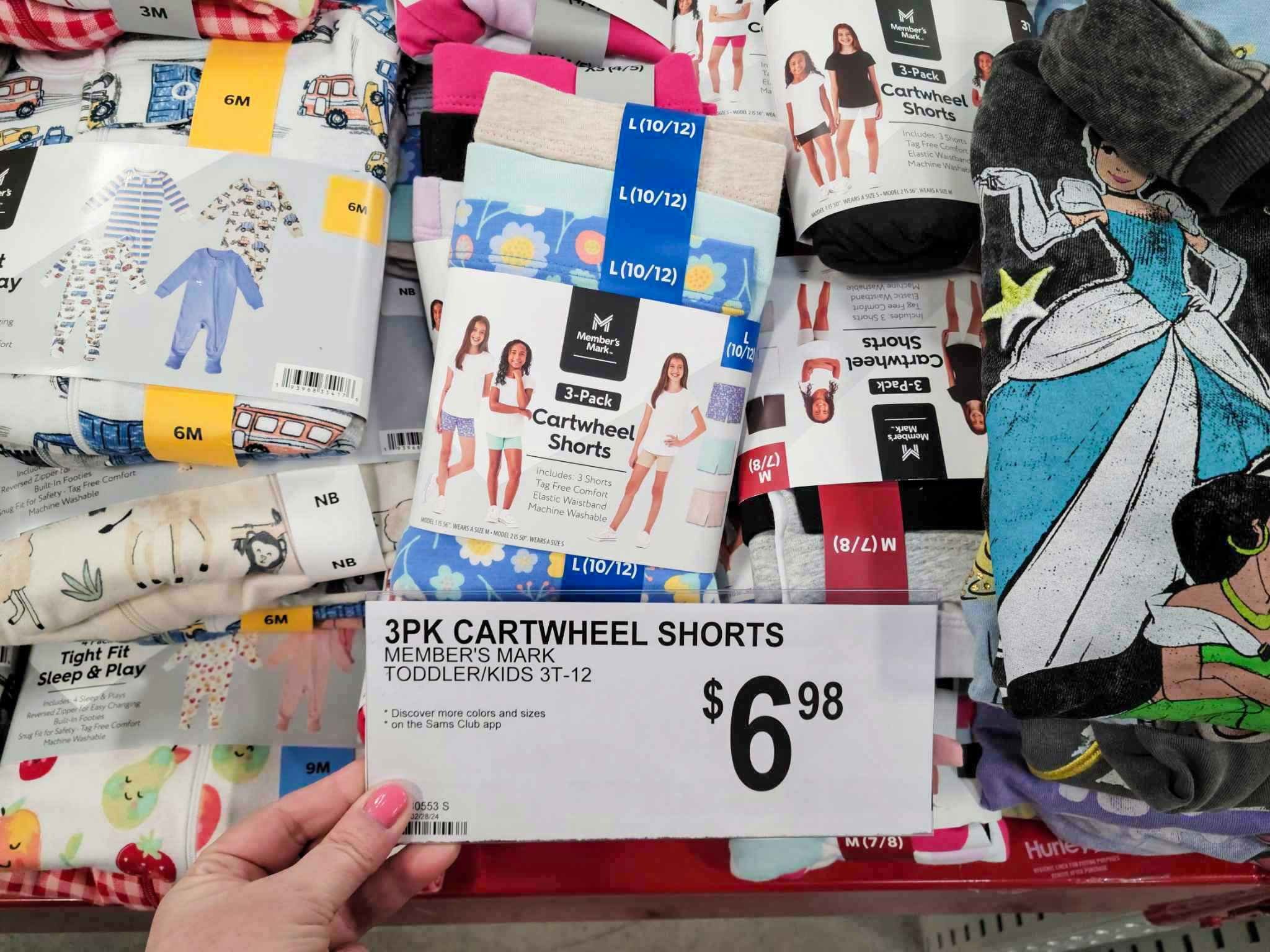 person holding a price sign for $6.98 3-packs of cartwheel shorts in front of a shelf of shorts