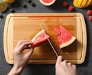 a person cutting a watermelon on a bamboo cutting board