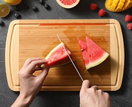 a person cutting a watermelon on a bamboo cutting board
