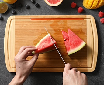 a person cutting a watermelon on a bamboo cutting board