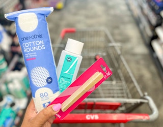 hand holding one+other cotton rounds, emery boards, and nail polish remover in front of shopping cart