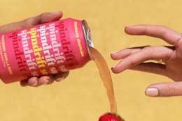 a person pouring a pink can of soda 