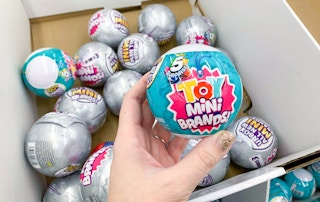 Someone picking out a 5 Surprise Mystery toy out of a box of them at Walmart