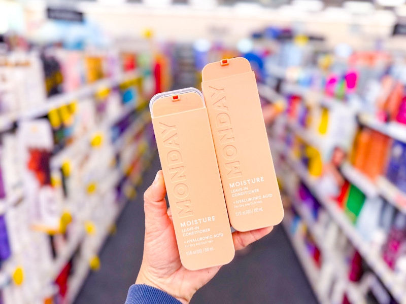 person holding 2 monday leave-in conditioners in an aisle