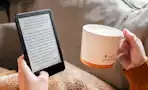a person holding a kindle and a cup of coffee