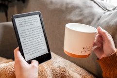 a person holding a kindle and a cup of coffee