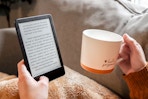 a person holding a kindle and a cup of coffee