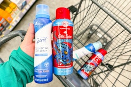 person holding secret and old spice spray deodorants over a cart