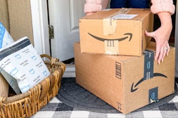 A person picking up Amazon boxes from a porch.