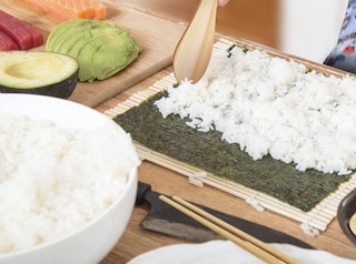 rice being spread on seaweed to be sushi