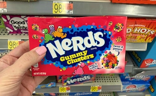 hand holding a movie theater box of nerds gummy clusters in front of walmart candy shelves