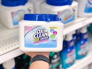 hand holding tub of tubs of Oxi Clean sanitizer in front of store shelf