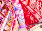 hand holding a barbie reveal toy in front of a target cart