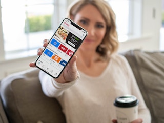 a person holding a phone out in front of her, facing the camera, with the ibotta app open on it.