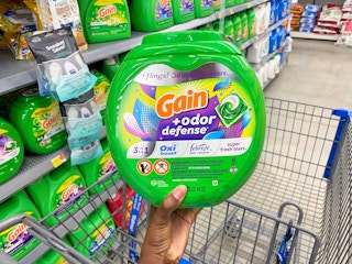 A bottle of Gain Flings Laundry Detergent held over a Walmart shopping cart