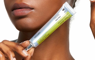 a hand holding a silver tube of skincare treatment 