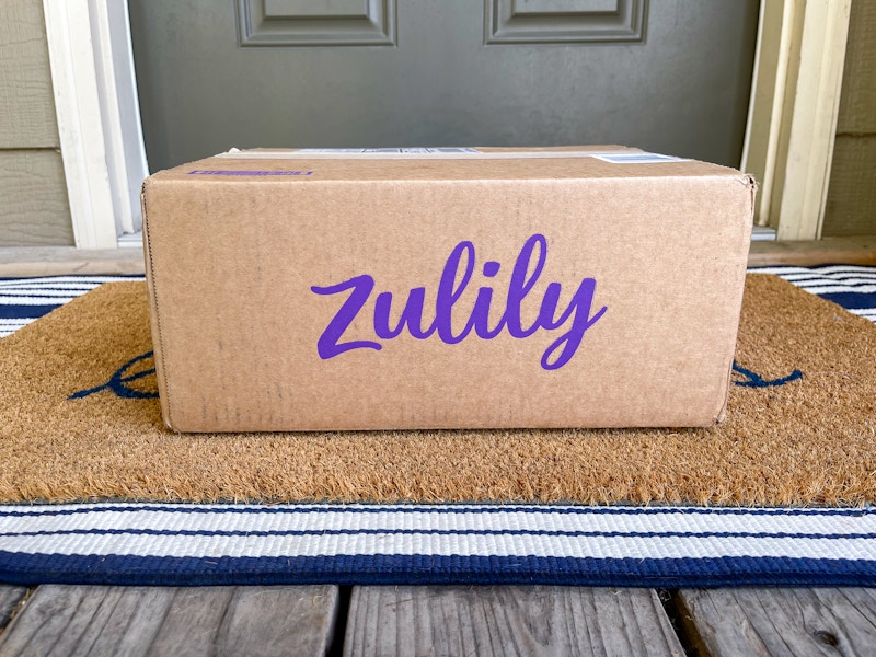 A Zulily box sitting on a front porch in front of someone's front door.