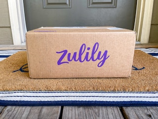 A Zulily box sitting on a front porch in front of someone's front door.