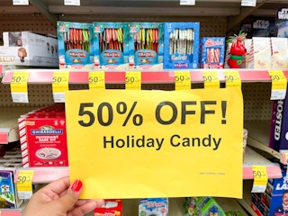 hand holding 50% Holiday Candy clearance signage in front of shelves