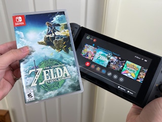 Someone holding a Legend of Zelda Tears of the Kingdom game next to a Nintendo Switch